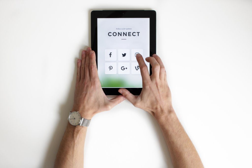 Man’s hands holding a tablet displaying social media icons.