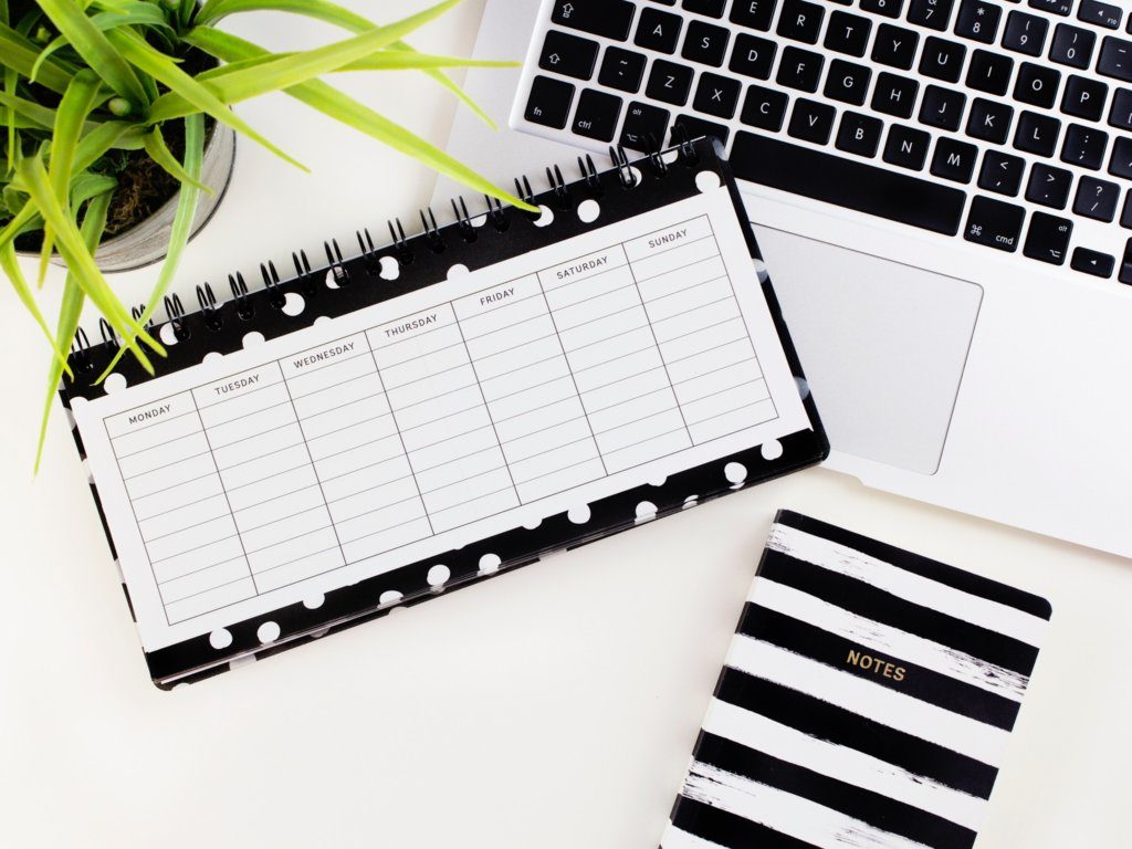 A blank weekly calendar sitting next to a laptop and a notebook.