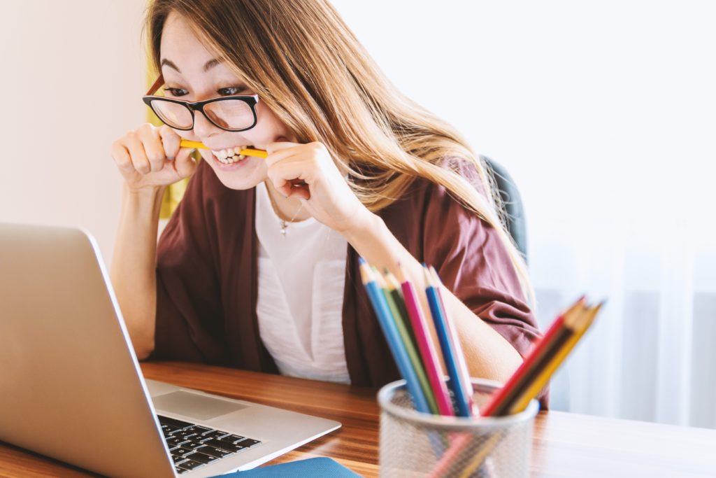 Woman biting a pencil as she looks at her laptop struggling with writing blogs for her business.