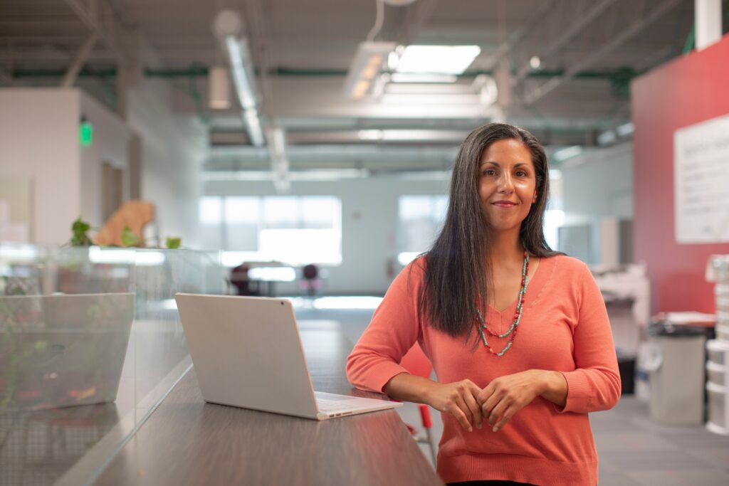 Business owner contemplating hiring an SEO consultant while standing next to her laptop in the middle of her office space.