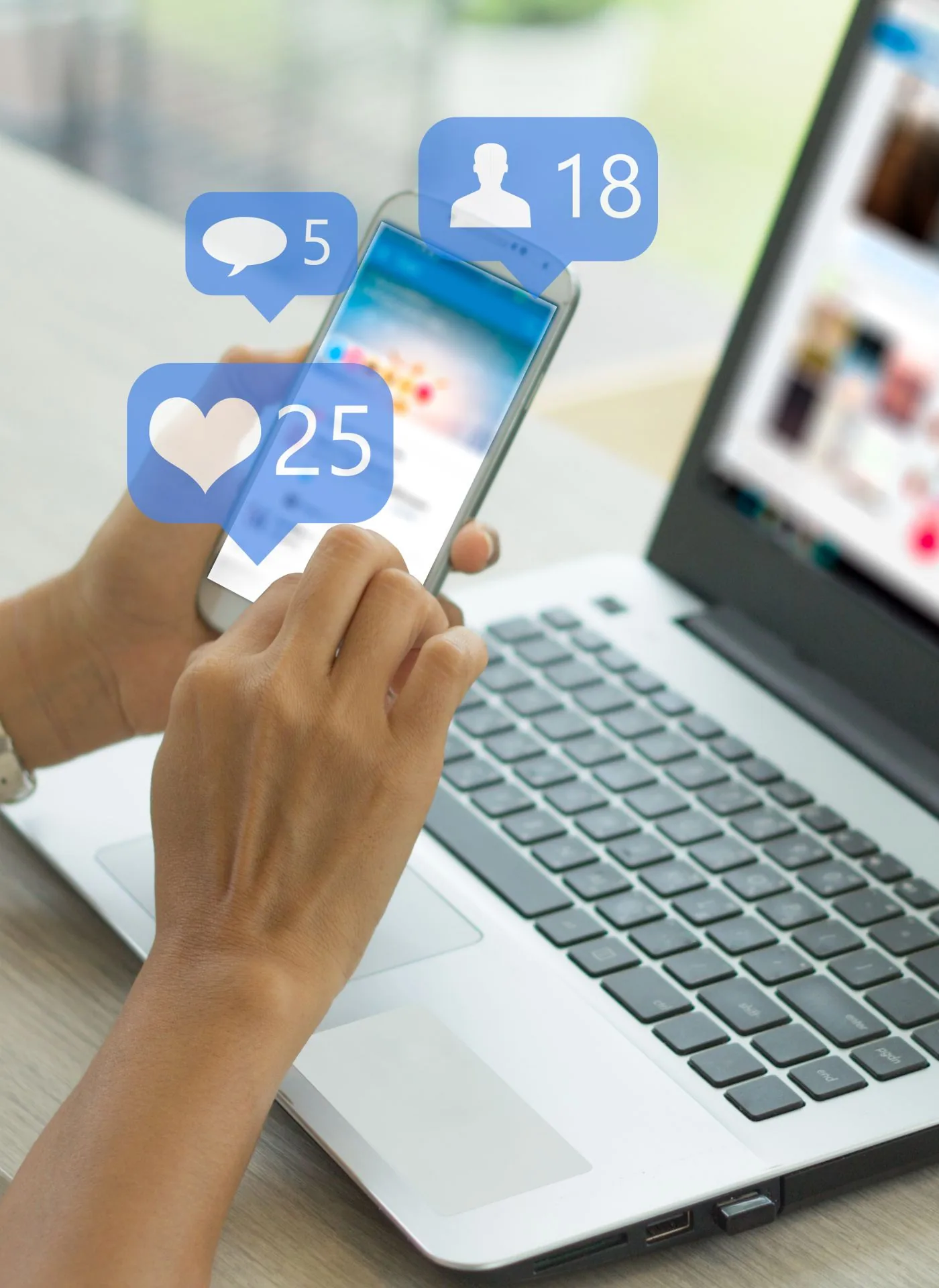 Hand holding smartphone displaying social media engagement icons showing 5 comments, 18 followers, and 25 likes, with laptop in background
