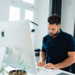Man standing at his computer thinking about how to implement SEO tips and tricks.