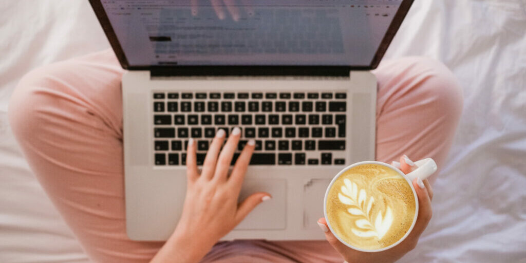 Woman using an SEO checklist for blog posts while she's blogging and holding a cup of coffee.