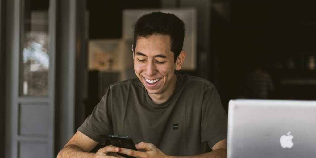 Man happily texting instead of blogging on the laptop open next to him.