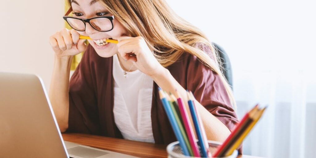 Woman biting a pencil as she looks at her laptop struggling with writing blogs for her business.